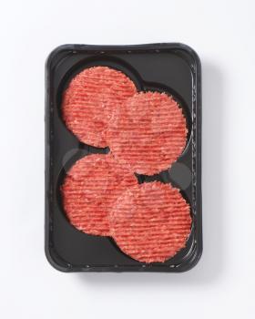 four raw hamburger patties on black plastic tray