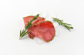 slices of green pepper coated salami with rosemary on white background