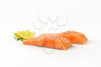 Two raw salmon fillets and lemon on white background
