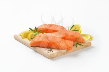 three raw salmon fillets, lemon and rosemary on cutting board