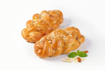 two loaves of sweet braided bread with almonds and raisins on white background