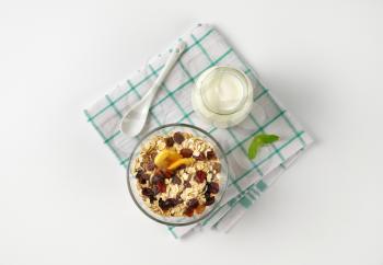 bowl of oat flakes and glass of white yogurt on checkered dishtowel