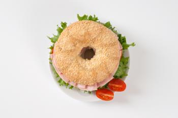 sesame bagel sandwich with ham on white plate