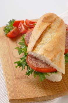 French loaf sandwich with salami on wooden cutting board