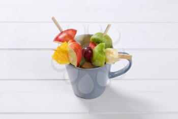 cup of fresh fruit skewers on white wooden background