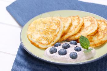 plate of american pancakes with yogurt and fresh blueberries on blue place mat - close up
