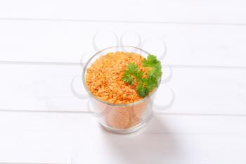 glass of peeled red lentils on white wooden background