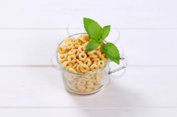 cup of honey cereal rings on white wooden background