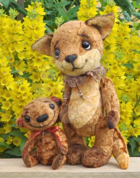 Teddy bear and fox cub on a board among flowers. Handmade, the sewed plush toys