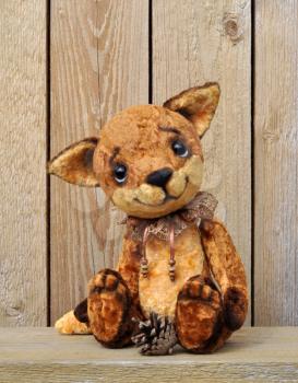 Ron fox cub on the background of a wooden plank wall with a pine cone. Handmade, the sewed plush toy