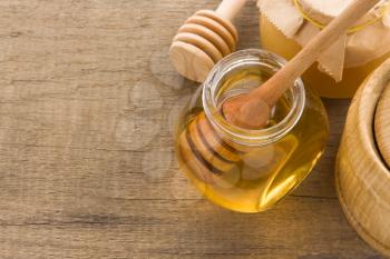 glass jar full of honey and stick on wood background
