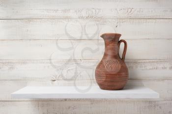 clay jug at shelf on white wooden plank background
