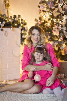 Portrait of mother with daughter near the Christmas sparkling lights of the Christmas tree and the fireplace.