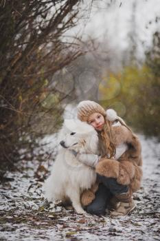 A child hugging and petting his white shaggy dog is a Samoyed.
