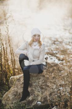 Beautiful girl resting on a huge stone on a background of a winter road.