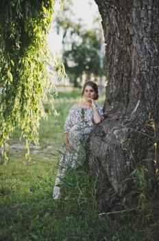 A beautiful portrait of a pregnant girl near a fallen branch of a weeping willow tree.