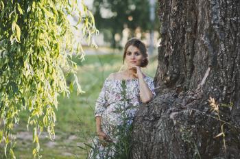 A beautiful portrait of a pregnant girl near a fallen branch of a weeping willow tree.