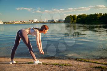 beautiful red-haired girl doing exercises on the river. against the backdrop of the city