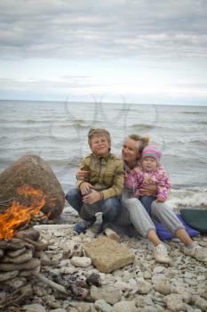 Mother with children on the sea in the fall sitting around the campfire .