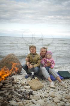 Mother with children on the sea in the fall sitting around the campfire .