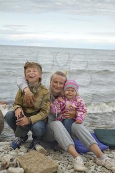 Mother with children on the sea in the fall sitting around the campfire .