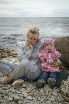 mother and daughter at the sea in the fall sitting around the campfire .