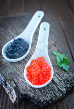 red and black caviar in white spoon and on a table