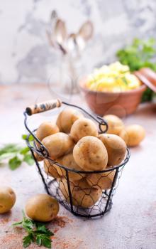 raw potato in metal basket and on a table