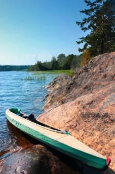 Canoe at camp on the shore of the beautiful lake at summer day under blue sky with light clouds