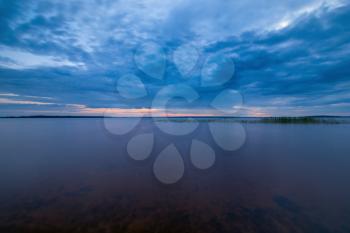 Blue tranquil minimalist landscape with smooth surface of the lake with calm water with horizon under dramatic cloudy sky, simple beautiful calm natural blue background