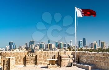Bahrain Flag with skyline of Manama at Bahrain Fort. A UNESCO World Heritage Site in the Middle East