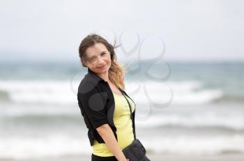 Young smiling woman standing sideways posing on a blurred background of ocean waves. Shallow depth of field. Focus on model.