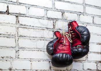 A pair of old boxing gloves hanging on white brick wall background.