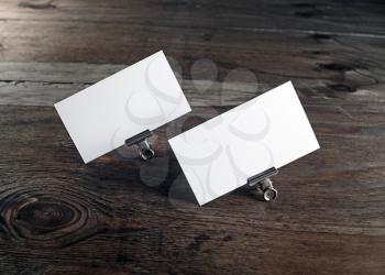 Two blank business cards in paper clips on dark wooden background. Blank template for ID. Mock-up for design presentations and portfolios.