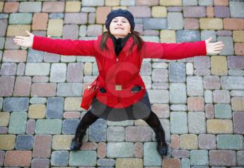 Happy girl. Pretty young smiling woman in a red jacket and beret is standing with arms outstretched and looking up.