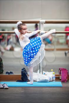 Child girl practicing in a ballet school with wooden floors on the background of mirrors. Little girl ballerina posing at ballet barre in a dance class. Shallow depth of field. Selective focus.