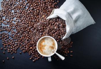 Espresso, coffee cup and coffee beans in a canvas bag on black wooden table background. Top view.