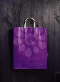 Blank purple paper shopping bag on wood table background. Flat lay.