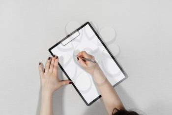 Woman writes on blank white sheet of paper. Clipboard in female hands. Flat lay.