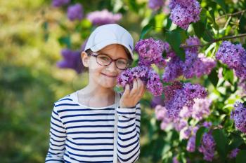 Smiling little girl smelling lilacs in the garden. Beautiful spring day. Selective focus.