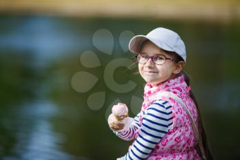 Smiling little girl with ice-cream in hands outdoors.