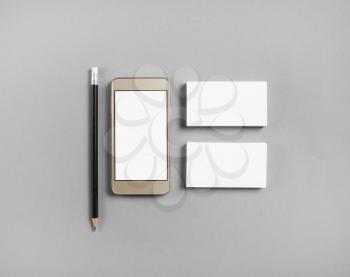 Mockup of blank business cards, pencil and cellphone with blank screen at gray paper background. Top view.