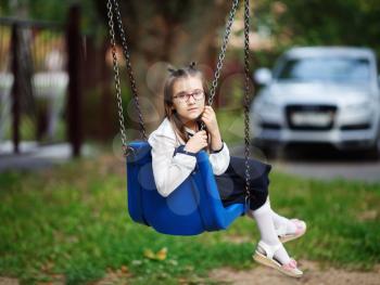 Child girl sitting on swing. Schoolgirl posing on the playground. Selective focus.