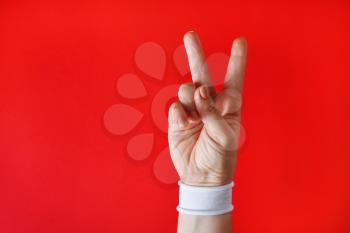 Female hand with white bracelet shows victory sign on red backgroung.