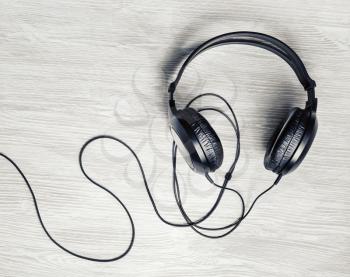 Photo of black dj stereo headphones on light wooden background. Flat lay.