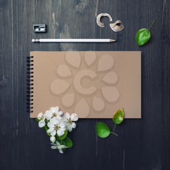 Blank closed sketchbook, pencil, sharpener and flowers and spring flowers on wood table background. Blank stationery set. Flat lay.