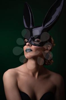 Sexy woman with a Easter bunny black mask standing on a dark background and looks sensually