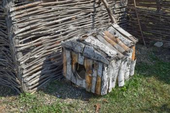 Doghouse birch near woven fence. Small house for a dog.