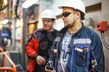 Workers in protective clothing and white helmets. A worker with a walkie-talkie in his hand.