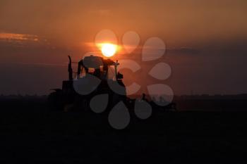 Tractor plowing plow the field on a background sunset. tractor silhouette on sunset background.